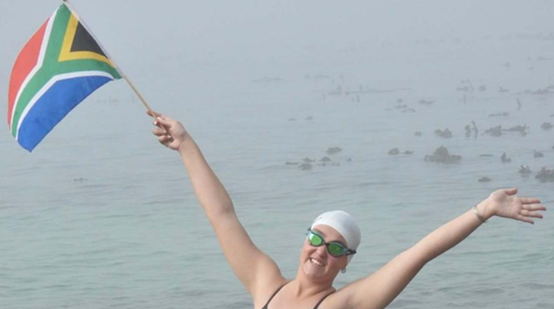 South African open-water swimmer celebrating with national flag after a swim