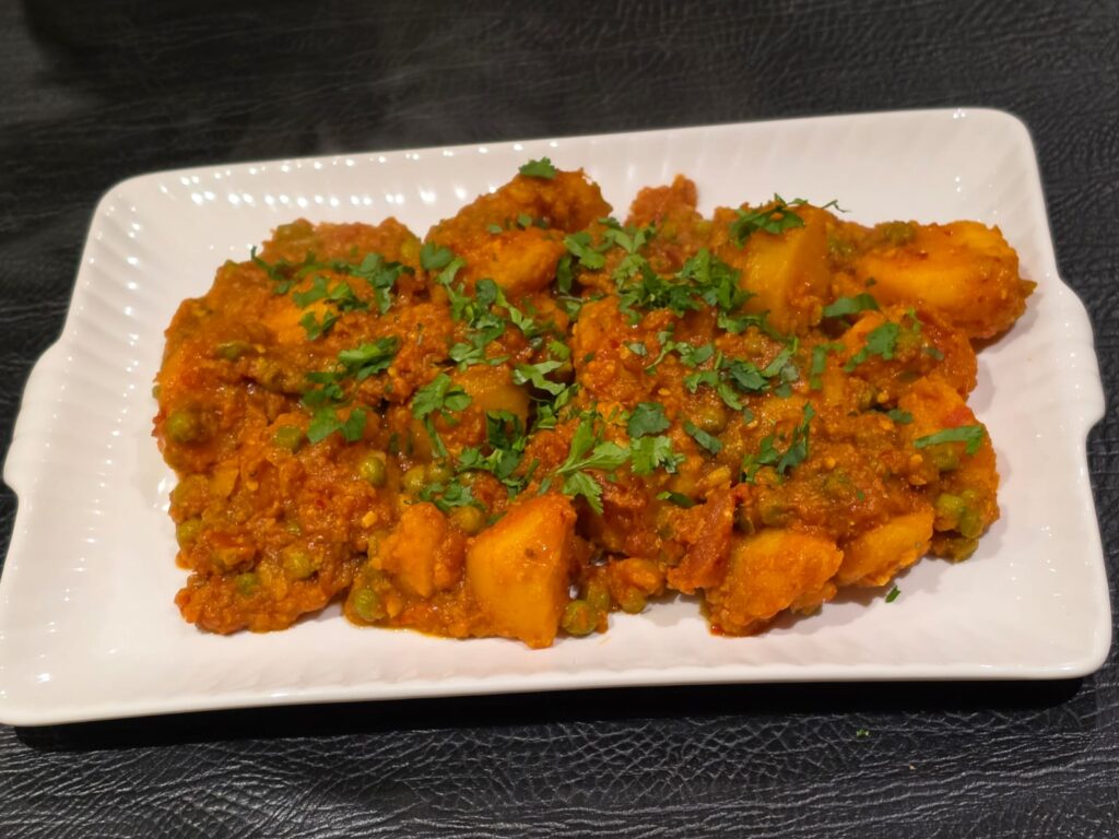 Potato and pea curry garnished with fresh coriander on a white platter