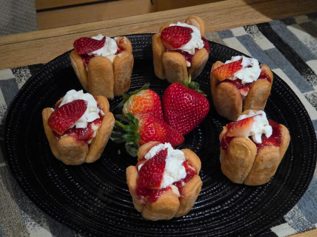 Finger biscuit cheesecake cups with strawberry topping on a black plate